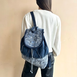 Peut inclure: Un sac à dos en jean bleu avec un rabat à motif blanc et bleu. Le sac à dos a une fermeture à cordon et des bretelles réglables.