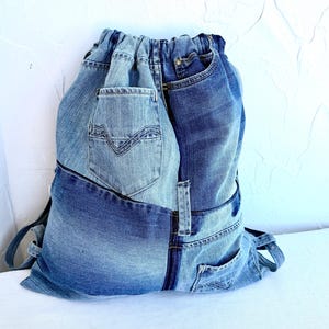 Op de afbeelding: Een rugzak met trekkoord gemaakt van gerecyclede spijkerbroeken. De tas heeft verschillende tinten blauwe denim, met zichtbare zakken en naden. Hij heeft schouderbanden en een trekkoordsluiting.