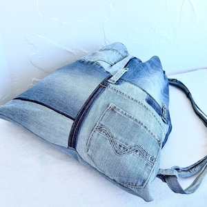 Op de afbeelding: Een denim tote bag gemaakt van gerecyclede jeans. De tas heeft een patchwork ontwerp met verschillende tinten blauw denim, inclusief zakken en naden. De bandjes zijn gemaakt van hetzelfde denim materiaal.