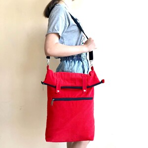 May include: A bright red rectangular crossbody bag made of corduroy fabric. The bag features a fold-over top flap with a black zipper closure, a secondary horizontal black zippered pocket on the front, and an adjustable black shoulder strap.