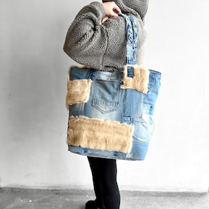 Könnte beinhalten: Eine große Tragetasche aus blauen Jeansstoff-Flicken und beigen Kunstfell-Einsätzen. Die Tasche verfügt über einen geflochtenen Jeans-Henkel und sichtbare Jeans-Taschendetails. Das Design umfasst mehrere rechteckige Flicken aus hellblauem Jeansstoff.