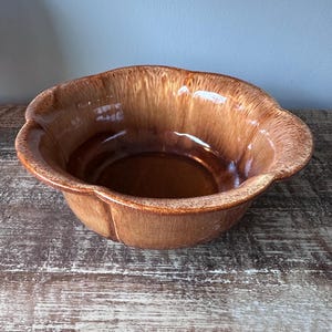 May include: A brown ceramic bowl with a scalloped edge. The bowl has a glossy finish and a light brown glaze.