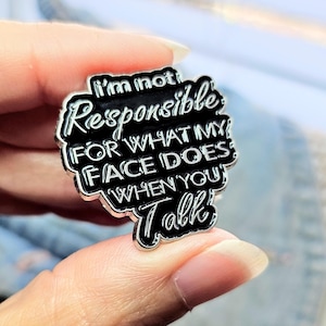 May include: A black and silver enamel pin with the text "I'm not responsible for what my face does when you talk".