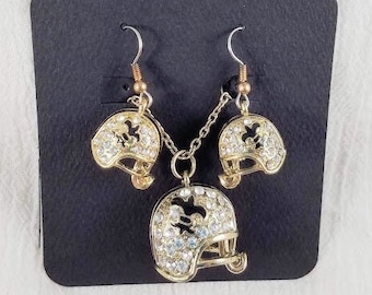 May include: A gold-tone necklace and earrings set featuring a football helmet design with clear rhinestones. The set is displayed on a black background.