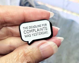 May include: A white enamel pin with a black border in the shape of a speech bubble. The pin says "The deadline for complaints was yesterday."