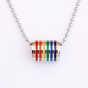 May include: A silver chain necklace with a rainbow colored pendant. The pendant is made of stacked rings with each ring a different color of the rainbow.