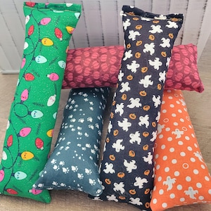 May include: A collection of cat toys in various patterns and colors. One toy is green with a string of colorful lights, another is navy blue with white paw prints, and a third is navy blue with white ghosts and orange pumpkins. Other toys have a red pattern and an orange and white polka dot pattern.