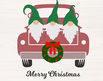 May include: Three gnomes in a red pickup truck with a green wreath and red bow. The truck has a white wooden background. The text "Merry Christmas" is below the truck.