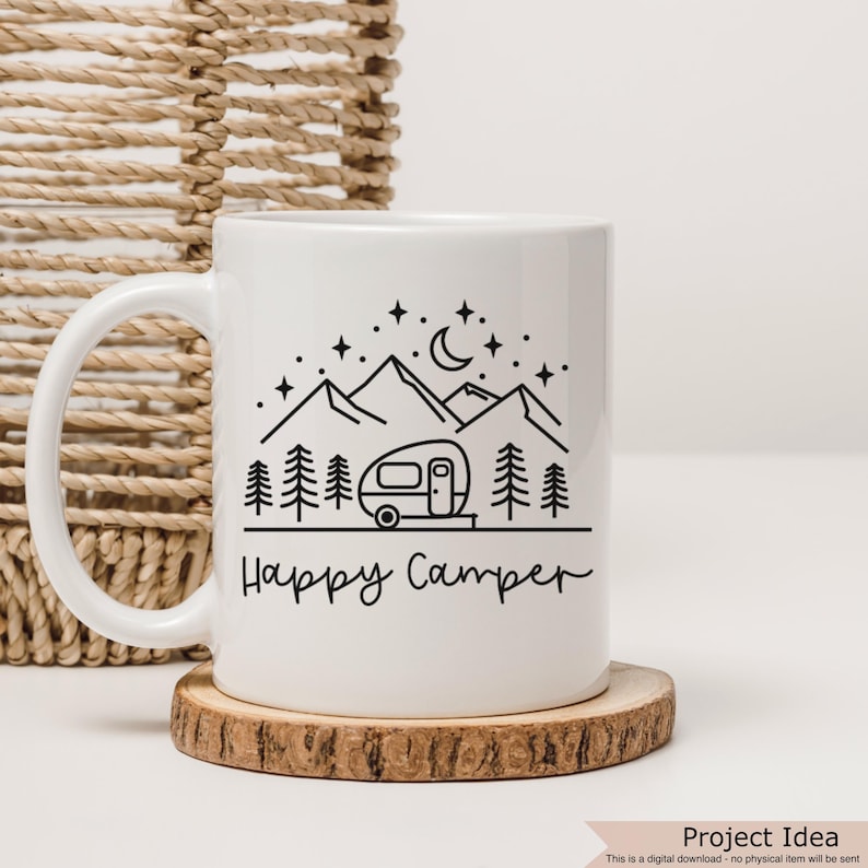 May include: White ceramic mug with a black line drawing of a camper, mountains, trees, and a crescent moon. The text "Happy Camper" is written in black cursive below the image.