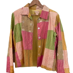 May include: A patchwork button-up shirt with long sleeves. The shirt is made of a variety of fabrics in shades of pink, green, yellow, and brown. The fabric is quilted and has a textured look. The shirt has a button-up front and a collar.