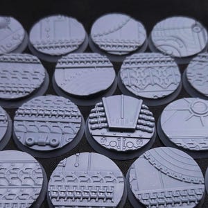 May include: A collection of gray, 32mm round bases with various textured designs. The bases feature intricate patterns, including mechanical and industrial elements, suitable for miniature figures. The bases are made of a durable material and are ideal for tabletop gaming.