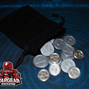 May include: A black velvet pouch spills out silver-colored metal tokens with various symbols, including stars and other geometric shapes. The pouch has a drawstring closure and is sitting on a blue patterned surface. The image also includes a logo for "Wargear Workshop".