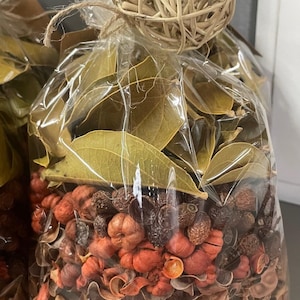 May include: A clear plastic bag filled with potpourri. The potpourri is a mix of dried leaves, flowers, and spices in shades of brown, orange, and red. A woven ball is tied to the top of the bag.