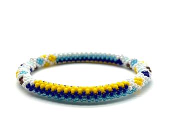 May include: A beaded bracelet with a spiral design. The bracelet features a pattern of yellow, blue, white, and brown beads. The bracelet is approximately 7 inches in circumference and is set against a white background.