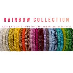 May include: A collection of 28 colorful bracelets arranged in a row, showcasing a rainbow of hues. The bracelets are numbered 1 through 28, with the text "RAINBOW COLLECTION" above them. The colors include silver, gold, orange, pink, blue, and green.
