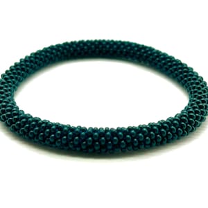 May include: A dark teal beaded bracelet made of small, round beads. The bracelet is a simple, elegant design.