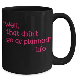 Puede incluir: Taza de café negra con una cita rosa que dice "Bueno, eso no salió como estaba planeado" -La vida.