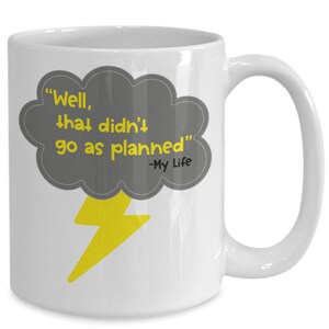 Puede incluir: Taza de café de cerámica blanca con un diseño de nube gris y rayo amarillo. La nube tiene el texto "Well, that didn't go as planned" con el texto "My Life" debajo.