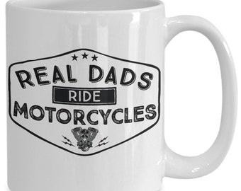 May include: White ceramic coffee mug with a black and white graphic design. The graphic features a vintage-style shield with the text "Real Dads Ride Motorcycles" and a motorcycle engine illustration.