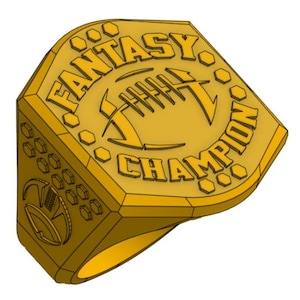Puede incluir: Anillo dorado con las palabras "FANTASY CHAMPION" y un diseño de fútbol americano. El anillo tiene un diseño geométrico con detalles hexagonales y circulares, sobre un fondo blanco.