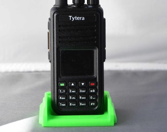May include: A black Tytera two-way radio with a green charging stand. The radio has a black antenna, a small screen, and a keypad with numbers and letters.