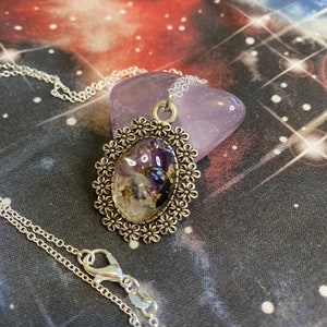 May include: A silver necklace with a pendant featuring a clear oval resin filled with amethyst, clear quartz, and gold flakes. The pendant is surrounded by a silver filigree design with small flower accents.