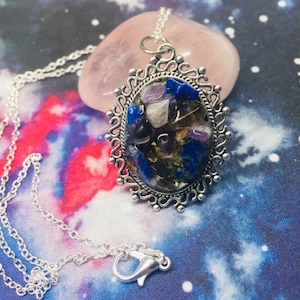 May include: A silver chain necklace with a silver oval pendant featuring a variety of colorful stones, including amethyst, lapis lazuli, and gold flakes, set in a clear resin.
