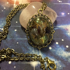 May include: A gold chain necklace with an oval pendant featuring a variety of iridescent green, brown, and purple stones set in a bronze filigree frame.