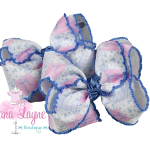May include: A large, decorative hair bow with a white, pink, and blue floral pattern. The bow has a blue trim and a matching blue center knot. The bow is a hair accessory.