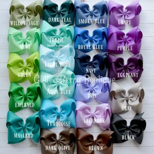May include: A collection of 20 large, handmade hair bows in various colors, including willow sage, dark teal, smoke blue, grape, mint, tropic, royal blue, purple, green, light blue, navy, eggplant, emerald, aqua blue, iris, gray, turquoise, lavender, mallard, dark olive, brown, and black. The bows are arranged in four rows of five bows each. The text "Glitter Berry Boutique" is visible in the center of the image.