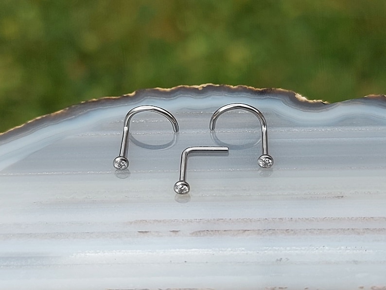May include: Three silver nose rings with clear gemstones. Two are curved and one is straight.