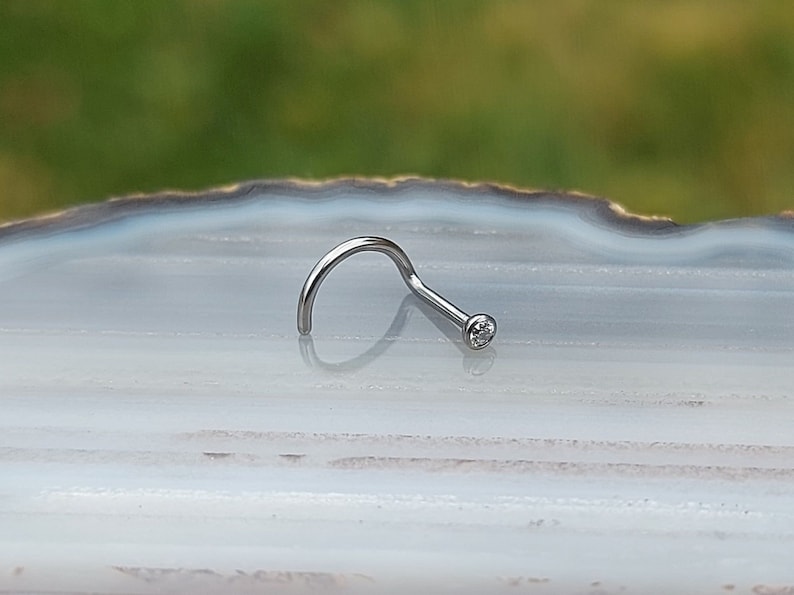 May include: A silver nose ring with a small clear gemstone.