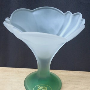 May include: A frosted glass ice cream sundae dish with a green base and stem. The bowl has a petal-like design. The base has the words "Strega Ice Cream" in gold lettering.