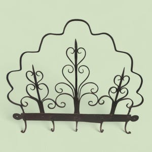 May include: A decorative wrought iron wall-mounted rack with a dark brown finish. The rack features an arched top with ornate scrollwork and three decorative floral elements. It has four hooks for hanging items.