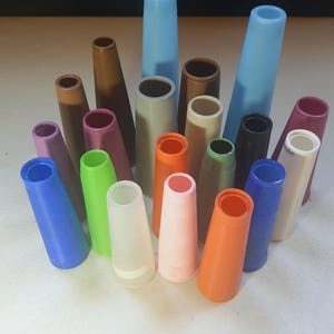May include: A collection of colorful, cone-shaped spools in various shades, including blue, brown, green, and orange. The spools are arranged in a group, showcasing their different sizes and hues. The spools are made of plastic.