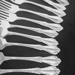 May include: A set of silver forks with ornate handles, arranged in a row on a black surface.