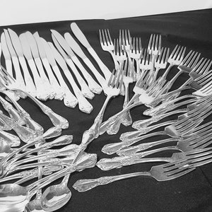 May include: A collection of silver flatware, including forks, knives, and spoons, arranged on a black surface.