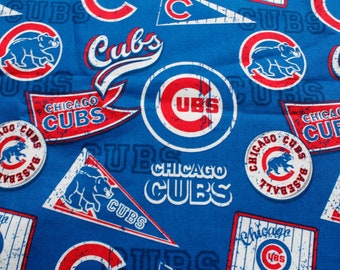 Może przedstawiać: Niebieska tkanina z wzorem logo i tekstu Chicago Cubs. Projekt zawiera logo niedźwiedzia drużyny, słowo "Cubs" w różnych czcionkach oraz słowa "Chicago Cubs Baseball". Loga są w kolorach czerwonym, białym i niebieskim.