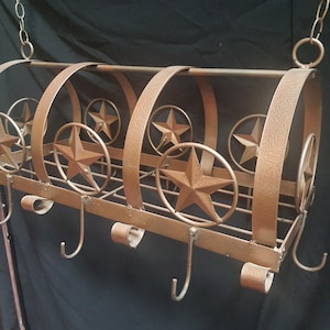 May include: A bronze-colored metal hanging basket with a Western theme. The basket features star cutouts and decorative hooks. The design includes a series of arched supports and a chain for hanging. The overall dimensions are approximately 18 inches wide.