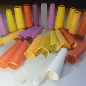 May include: A collection of colorful, cone-shaped sewing thread spools in various shades of yellow, orange, pink, purple, and white. The spools are made of plastic and are arranged in a scattered pattern, with some overlapping.