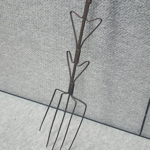 May include: A rustic, dark brown metal garden fork with four tines. The handle features decorative arrow-shaped designs. The tool is designed for gardening and landscaping tasks.