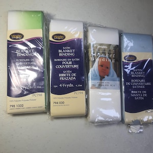 May include: Four packages of Wrights blanket binding in various colors. The packages include green ombre, white, and blue satin binding. Each package is labeled with the product name, material, and length.