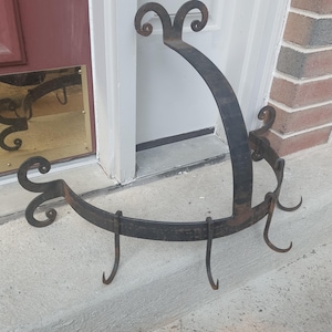 May include: A wrought iron wall-mounted coat rack with a curved design. The rack is dark brown with decorative scrollwork at the ends and top. It features several hooks for hanging items.