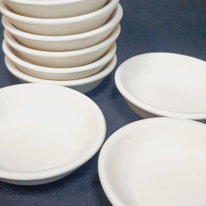 May include: A stack of six white ceramic bowls, with three additional bowls on a dark blue surface.