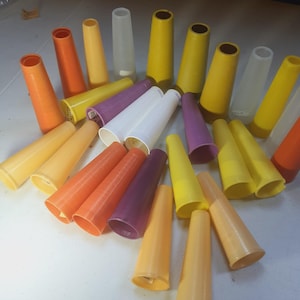 May include: A collection of colorful, cone-shaped plastic thread holders in shades of orange, yellow, purple, and white. The cones are arranged on a light-colored surface, showcasing their varying sizes and hues. These are likely used for organizing thread.