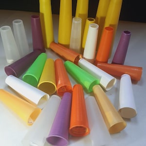 May include: A collection of colorful, cone-shaped plastic spools in various sizes and hues, including yellow, orange, green, purple, and white. The spools are arranged in a scattered pattern, with some standing upright and others lying on their sides.