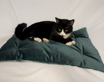 May include: A black and white cat with yellow eyes is lying on a dark green velvet pillow with tufted buttons.