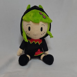 May include: Green and black plush toy with a black hooded jacket and green hair. The toy has a smiling face with black eyes and a red mouth.
