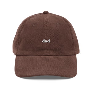 May include: A brown corduroy baseball cap with the word "dad" embroidered in white on the front.