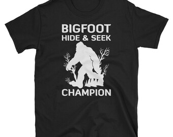 May include: Black t-shirt with white text that reads "BIGFOOT HIDE & SEEK CHAMPION". A white silhouette of Bigfoot is walking through a forest.